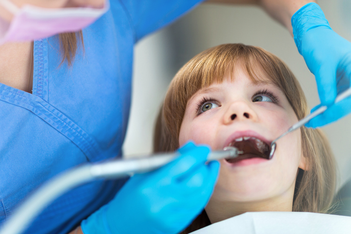A young girl sitting in a dentist's chair receiving a routine check up and teeth cleaning.