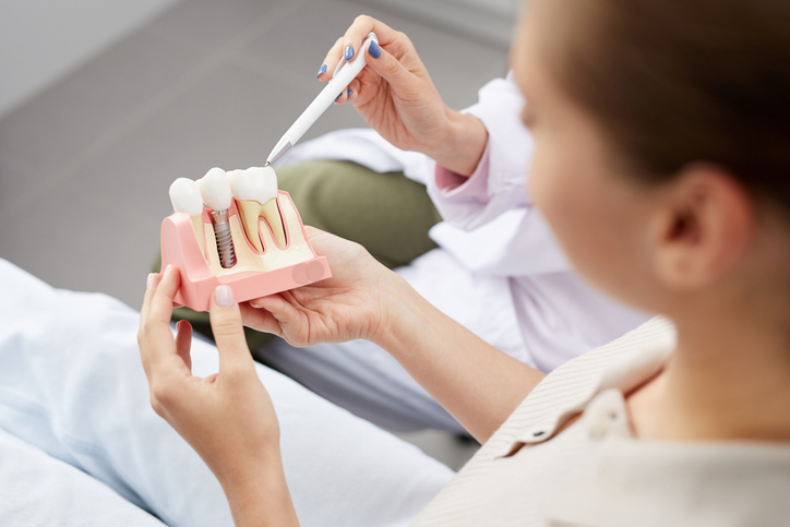 High angle view of unrecognizable young woman holding tooth model during consultation in dentists office.